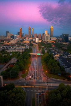 an aerial view of a city at dusk with cars driving on the road and buildings in the background