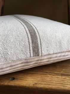 a pillow sitting on top of a wooden table next to a chair with a white and brown striped pillow