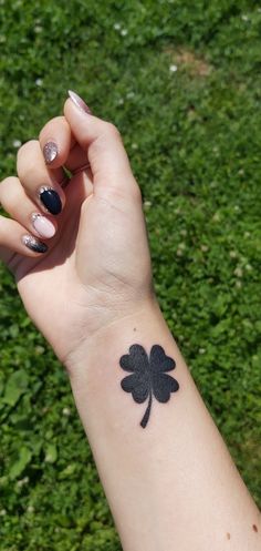 a woman's arm with a small black clover tattoo on it