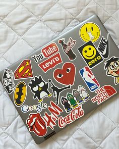 a laptop covered in stickers sitting on top of a white quilted bed cover