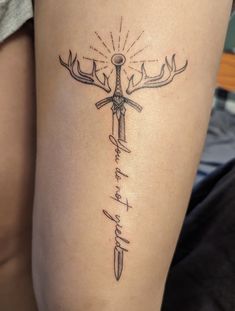 a cross tattoo on the thigh with words written below it and an antelope