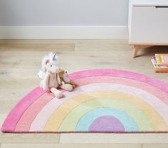 a stuffed animal sitting on top of a rainbow rug in a child's room