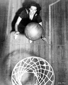 an old photo of a woman playing with a basketball in front of a hoop on the floor