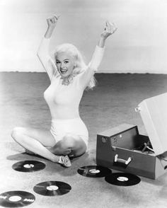 a woman sitting on the floor with her arms in the air, surrounded by records