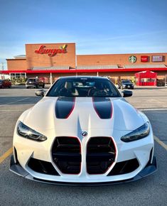 a white sports car parked in front of a building with red and black stripes on it