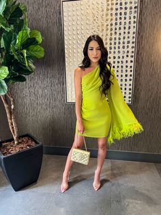 a woman standing in front of a wall holding a purse and wearing a yellow dress