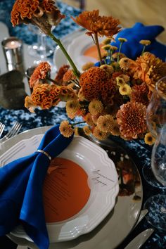 the table is set with orange flowers and blue napkins for an elegant centerpiece