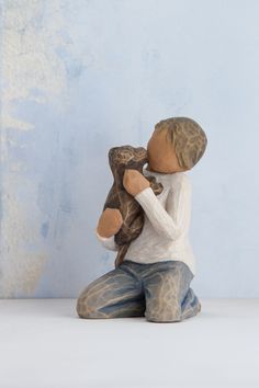 a ceramic figurine of a boy holding a teddy bear in his arms and sitting on the ground