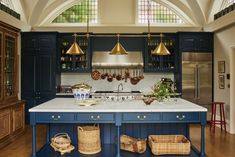 a large kitchen with blue cabinets and white counter tops, gold pendant lights over the island