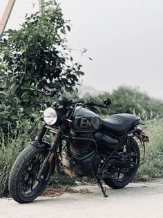 a motorcycle is parked on the side of the road near some bushes and trees in the background