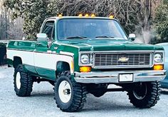 a green and white truck parked in front of a blue car with its lights on