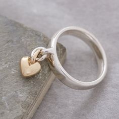 Add charm to your jewellery collection with our exquisite and unique solid silver ring, adorned with a delicate sweetheart recycled gold heart charm that gracefully sways with your every move. This everyday yet extraordinary ring is destined to spark conversations and become a cherished part of your personal style. Craftsmanship: Meticulously crafted using traditional lost wax casting techniques, our solid sterling silver rings are designed for both aesthetics and comfort. The ring features a robust and enduring loop on the front, while its generous band shape prioritizes comfort, durability, and contemporary elegance. The dangling heart charm is crafted from your choice of either recycled solid rose gold, or recycled solid yellow gold, with a beautifully rounded, organic shape. Quality As Ring With Charms, Charm Rings Dangle, Chunky Silver Rings, Charm Ring, Gold Heart Ring, Unusual Rings, Silver Signet Ring, Rose Gold Heart, Designer Fashion Jewelry