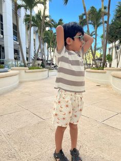 a little boy standing on the sidewalk with his arms behind his head and palm trees in the background