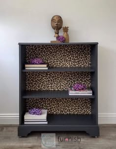 a black bookcase with leopard print on it and purple flowers in the middle, against a white wall