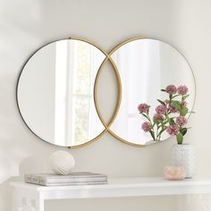 two round mirrors on the wall above a white table with pink flowers and a vase