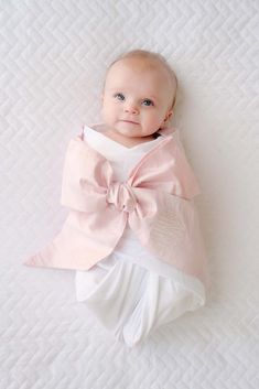 a baby wrapped in a pink bow laying on top of a white bedding sheet