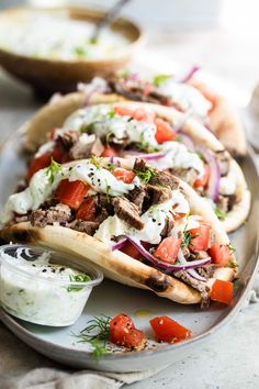 two pita sandwiches on a plate topped with meat, tomatoes and sour cream sauce