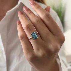 a woman wearing a ring with an aqua blue topazte on it's finger