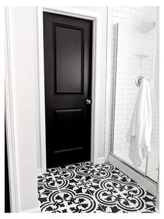 a bathroom with black and white tile flooring next to a shower door, towel hanging on the wall