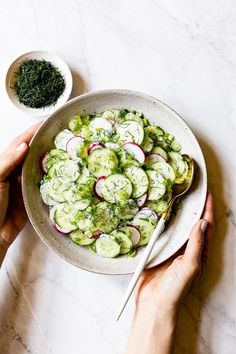 a white bowl filled with cucumbers and radishes next to a spoon