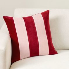 a red and white striped pillow sitting on top of a white couch next to a wall