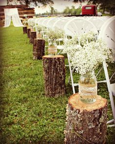 an outdoor ceremony with white flowers in vases and wooden stumps on the grass