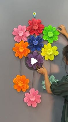 a woman is making colorful paper flowers on the wall with her hands and holding a video game controller