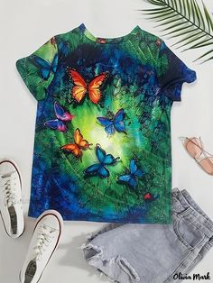 a t - shirt with butterflies on it next to shoes and palm tree leaves in the background