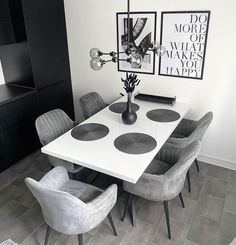 a dining room table with chairs and pictures on the wall above it, in front of a black cabinet