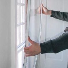 a woman is opening the curtains in front of her window and pointing at it with both hands