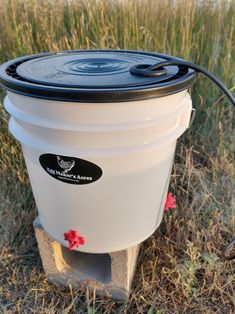 a white bucket sitting on top of a field next to a water pump and hose