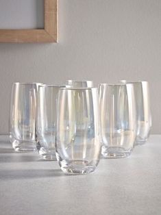 six clear wine glasses lined up on a white countertop next to a framed photograph