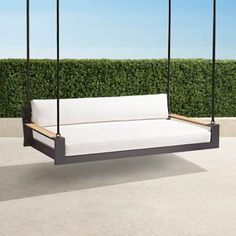 a white couch sitting on top of a wooden swing bed next to a green hedge