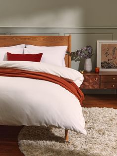 a bed with white and red pillows on top of it next to a wooden dresser