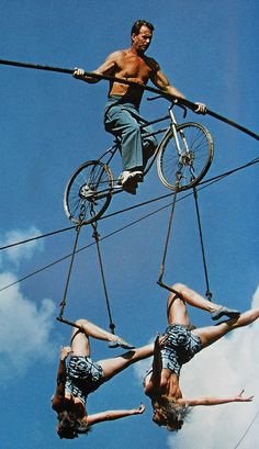 a man riding a bike on top of two women upside down in the air with their hands