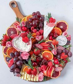 a platter filled with fruit and cheese on top of a white countertop next to a wooden cutting board