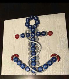 an anchor made out of bottle caps on a piece of white paper with red and blue buttons