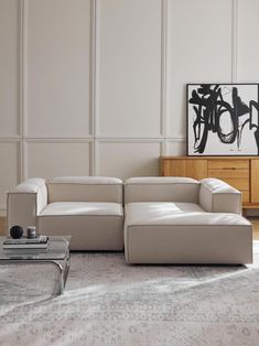 a modern living room with white walls and beige leather couches, coffee table and art on the wall