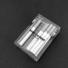 four white candles are in a clear box on a black surface with the words saint laurent printed on it