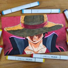 some markers are laying on the table next to a drawing of one piece of anime character