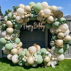 a happy birthday balloon arch with balloons and greenery on the front lawn at a backyard party