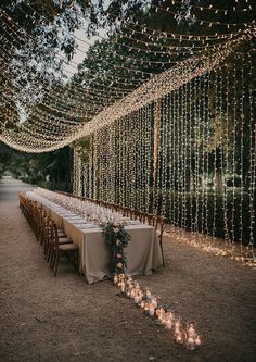 a long table set up with candles and greenery for an outdoor wedding reception in the woods