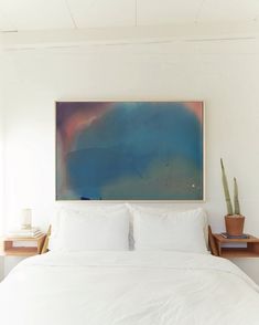 a bed with white sheets and pillows in a bedroom next to a painting on the wall