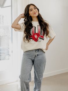 a woman standing in front of a window wearing jeans and a t - shirt with the letter u on it