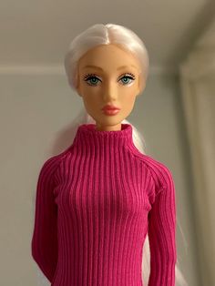 a barbie doll wearing a pink sweater and white hair is standing in front of a wall