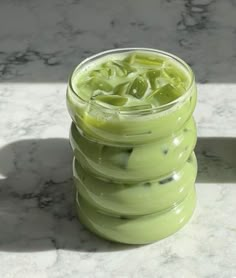 a glass filled with green liquid sitting on top of a marble counter next to a bottle