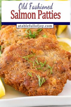 two fried salmon patties on a white plate with lemon wedges and rosemary garnish