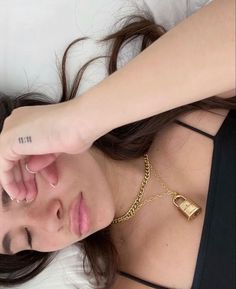 a woman laying on top of a bed wearing a black tank top and gold chain necklace