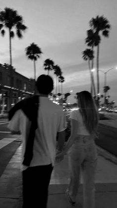 a man and woman walking down the street at night with palm trees in the background