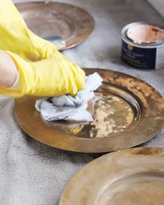 a person in yellow gloves wiping up some paint on a gold plate with a brush